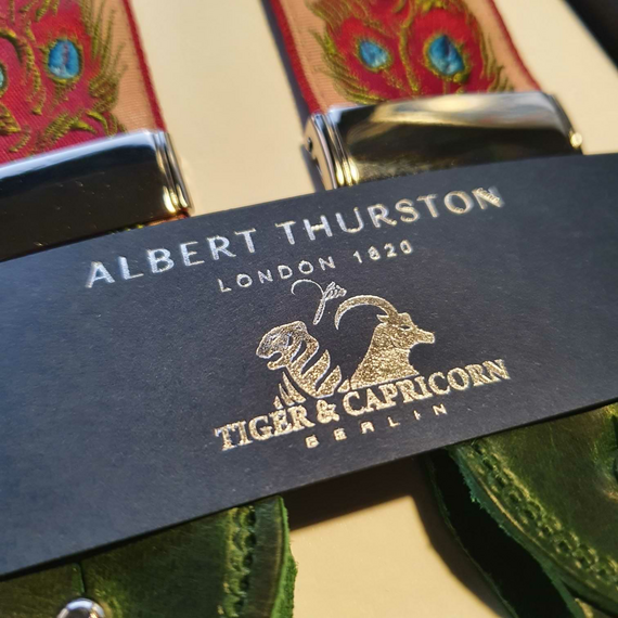 Hosentrger von Albert Thurston fr Tiger & Capricorn mit Pfauenfedern in Rot und Blau. Die Lederteile sind passend in Dunkelgrn gehalten.
