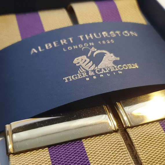 Ein Albert Thurston Hosentrger mit Bndern in Violett und Gold, violettem Leder, goldenen Verstellern und geflochtenen Laschen in Schwarz ist im Ausschnitt schrg von der Seite zu sehen.